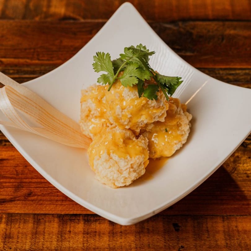 Four crispy fried shrimp balls with orange sauce and cilantro on a white plate.